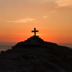 Kamienny krzyż na skalistym wzgórzu o zachodzie słońca, symbolizujący moment, kiedy umarł Jezus.