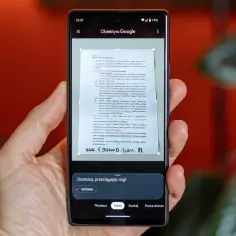Ręka trzyma telefon, na ekranie którego działa skaner w telefonie, skanując dokument.