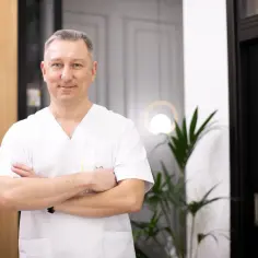Mężczyzna w białej koszuli lekarskiej ze skrzyżowanymi rękami, uśmiechnięty.