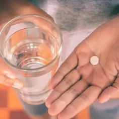 Dłoń trzyma szklankę wody i tabletkę. Uważaj, paracetamol dawka śmiertelna jest niebezpieczna.