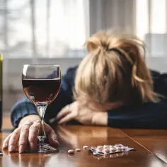 Kobieta z opuszczoną głową obok kieliszka wina i leków. Niebezpieczne połączenie escitalopram a alkohol.