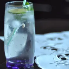 Orzeźwiający martini ze spritem, z lodem, plasterkiem limonki i miętą, w szklance z fioletową podstawą.