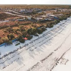 Widok z lotu ptaka na tropikalną plażę z białym piaskiem i zieloną roślinnością. Zastanawiasz się, jak długo trwa lot na Zanzibar z Polski?