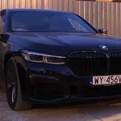 Eleganckie, czarne BMW 750i z charakterystycznym grillem i nowoczesnymi światłami, zaparkowane przy metalowym ogrodzeniu.