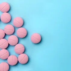 Różowe tabletki ketrel 100 mg ułożone na niebieskim tle.