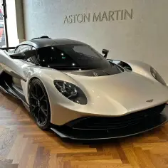 Srebrny Aston Martin na drewnianej podłodze. Zastanawiasz się nad aston martin cena?