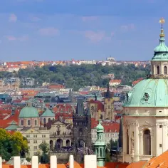 Widok na Pragę z zielonymi kopułami i charakterystyczną wieżą telewizyjną w tle.