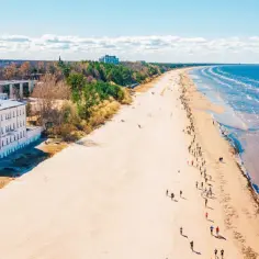 Szeroka, piaszczysta plaża nad Bałtykiem, z ludźmi spacerującymi i budynkami w tle. Potwierdza to, że Łotwa ma dostęp do morza.