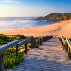 Drewniane schody prowadzą na piaszczystą plażę nad oceanem. To dowód, że Portugalia leży nad morzem, oferując piękne widoki.
