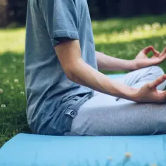 Osoba medytuje na trawie, pokazując, jak się zrelaksować psychicznie.
