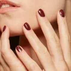 Dłonie z idealnym, ciemnoczerwonym manicurem kombinowanym, dotykające delikatnie twarzy.
