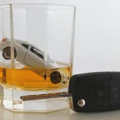 Szklanka z whisky, w której pływa model samochodu, obok kluczyki. Ile trzyma 250 ml wódki, tyle może kosztować utrata prawa jazdy.