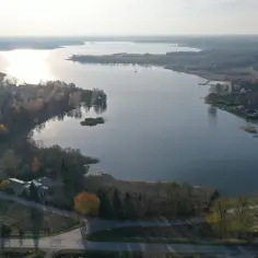 Jesioro Kałębie w jesiennej odsłonie, z widokiem na spokojną taflę wody, otoczoną drzewami w barwach złota i czerwieni.