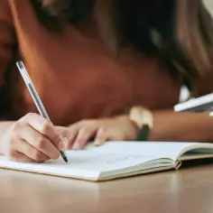 Osoba pisze w notatniku, tworząc zdania z przestawnym szykiem, by lepiej wyrazić swoje myśli.