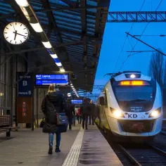 Pasażerowie czekają na pociąg na dworcu PKP Jelenia Góra. Zegar wskazuje 06:27, a tablica informuje o odjeździe do Legnicy.