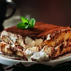 Pyszne tiramisu bez alkoholu, udekorowane kakao i miętą, na białym talerzu.