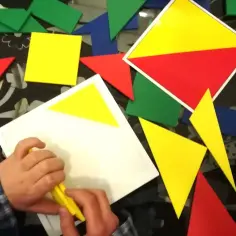 Dziecko układa kolorowe **wzory geometryczne** z klocków tangramu na czarnym tle.
