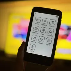 Smartfon z ikonami aplikacji: aparat, dyktafon, e-czytnik, kalkulator, mapy, medytacja, muzyka, notatki, pogoda, szachy. Tło to rozmyty ekran telewizora.