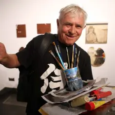 Uśmiechnięty Piotr C. Kowalski, artysta z pędzlami w butelce, prezentuje swoje prace.