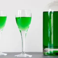 Dwa kieliszki i butelka wypełnione jaskrawozielonym likierem miętowym, idealne do domowego przepisu na zielony likier miętowy typu creme de menthe.