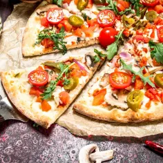 Pizza z pomidorami, jalapeno, pieczarkami i rukolą. Widać kolejność składników na pizzy: sos, ser, dodatki.