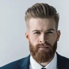 Mężczyzna w garniturze z gęstą, rudą brodą. Jego fryzura jest starannie ułożona, a spojrzenie intensywne. Broda u mężczyzn dodaje mu charakteru.