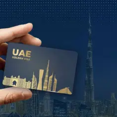Dłoń trzyma kartę "UAE GOLDEN VISA" na tle panoramy Dubaju z Burdż Chalifą.