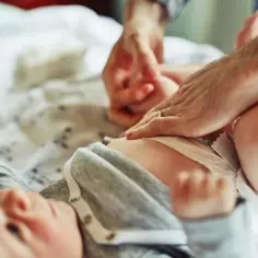 Rączki rodzica zmieniają pampersa noworodkowi. Ile noworodek zużywa pampersów? To pytanie nurtuje wielu rodziców.