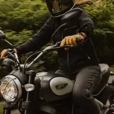 Motocyklista w kasku i rękawiczkach jedzie motocyklem po drodze. W tle zielone drzewa. To idealny moment, by nauczyć się, jak zmieniać biegi w motorze.