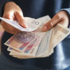 Dłonie liczą polskie banknoty. Zastanawiasz się, ile wzrośnie emerytura z OFE po 65 roku życia?