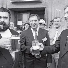 Trzech mężczyzn w garniturach wznosi kufle piwa. Wyglądają jakby świętowali powstanie polskiej partii przyjaciół piwa.