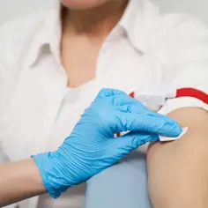 Ręka w niebieskiej rękawiczce dezynfekuje ramię przed pobraniem krwi do badania, które może pomóc w ocenie krzywej insulinowej.