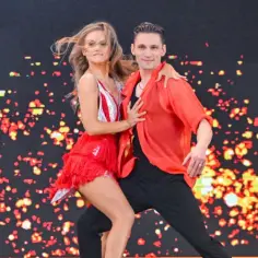 Kaczorowska w "Tańcu z Gwiazdami" w czerwonej, zwiewnej kreacji, tańczy z partnerem na tle migoczących świateł.