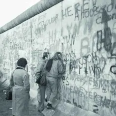 Ludzie oglądają graffiti na Murze Berlińskim, symbol upadku podziału.