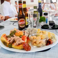 Malta jedzenie: talerz z tuńczykiem, kaparami, fasolą i pieczywem, obok piwo i okulary przeciwsłoneczne.