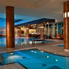 Basen w hotelu Radisson Blu Radebeul, z niebieską wodą, drewnianymi kolumnami i leżakami.