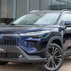 Ciemnoniebieski Toyota Corolla Cross z hybrydowym znaczkiem na grillu, zaparkowany przed nowoczesnym budynkiem.
