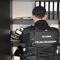 Funkcjonariusz Służby Celno-Skarbowej przegląda dokumenty w szafie. Kontrola skarbowa w toku.