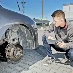 Mężczyzna sprawdza na tablecie instrukcję wymiany amortyzatorów tył przy samochodzie na parkingu.