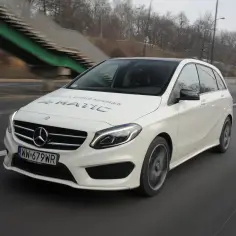 Biały Mercedes B180 4MATIC jedzie po drodze, za nim zielony wiadukt.