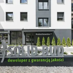 Nowoczesny budynek z napisem "SOLID-BUD deweloper z gwarancją jakości".