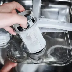 Dłoń wyjmuje filtr zmywarki, pokazując jak wyczyścić filtr w zmywarce.
