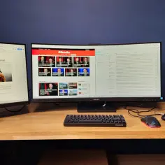 Dwa monitory i laptop z otwartymi oknami, klawiatura i myszka na drewnianym biurku.