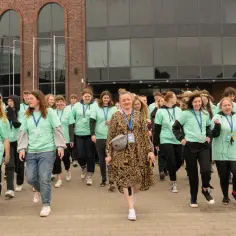 Grupa młodych ludzi w zielonych koszulkach z napisem "Szkoła w Chmurze" idzie przed ceglanym budynkiem.