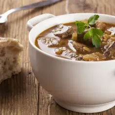 Pyszny gulasz wołowy w białej miseczce, z kawałkiem chleba i łyżką obok. Idealny na zimne dni, dowiedz się jak zrobić gulasz!