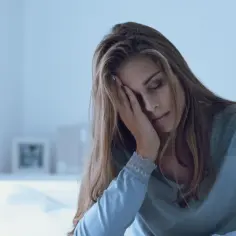 Zmęczona kobieta w łóżku, z ręką na twarzy, jakby po zażyciu mirtagenu.