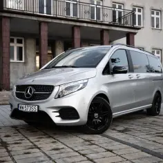 Srebrny Mercedes-Benz Klasy V z czarnymi felgami, zaparkowany przed budynkiem z balkonem.