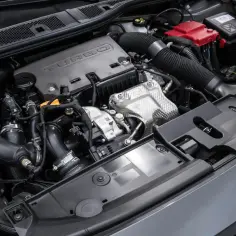 Silnik 1.2 PureTech z turbosprężarką w samochodzie Peugeot 208. Widoczne elementy układu dolotowego, akumulator i osłony.