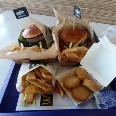 Dwa Maestro Burger McDonald's z frytkami i nuggetsy na tacy.