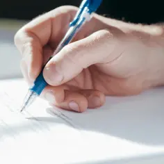 Dłoń pisze długopisem na dokumencie, być może podpisując pełnomocnictwo ogólne.